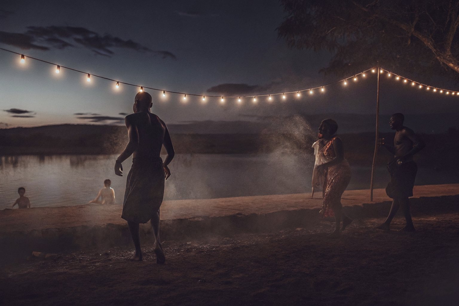 An open-air rave on a lakeside at night, lit by a string of warm bulbs